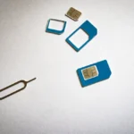 Różne rozmiary kart SIM i narzędzie do tacki SIM leżące na jasnym tle. Ilustracja problemu z niewykrywaną kartą SIM w telefonie.
